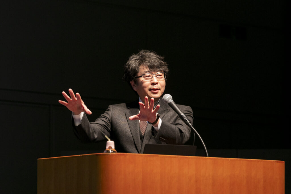 A man in a suit standing at a podium with his hands up