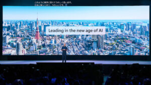 A man standing on a stage with a large screen with a city in the background