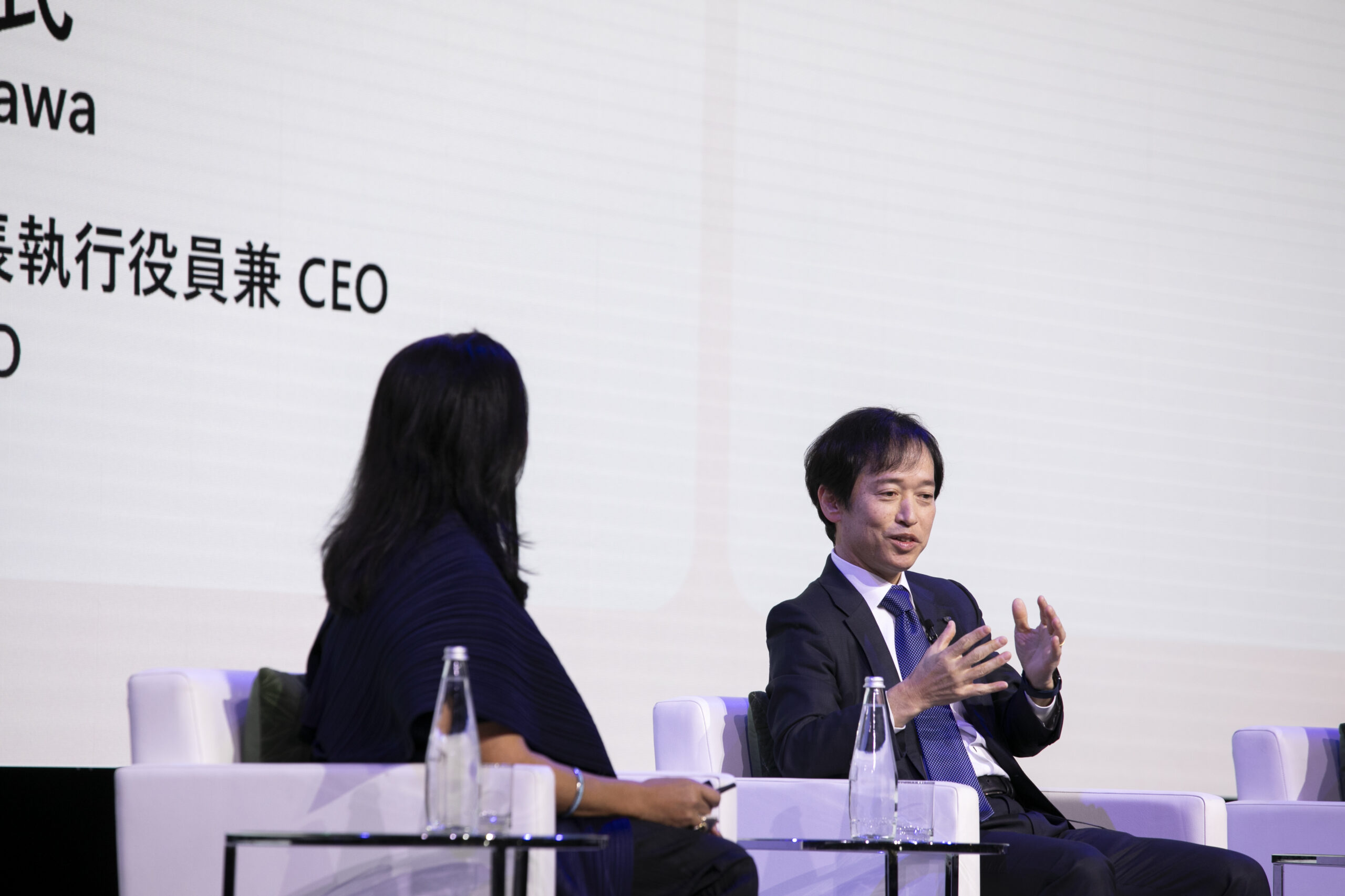 A man in a suit and tie talking to a woman in a white room