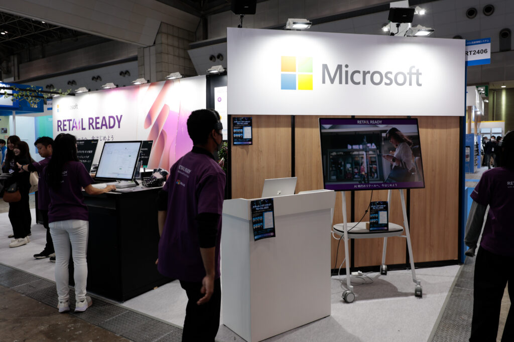 A man standing in front of a booth with a sign and a man standing in front of a computer