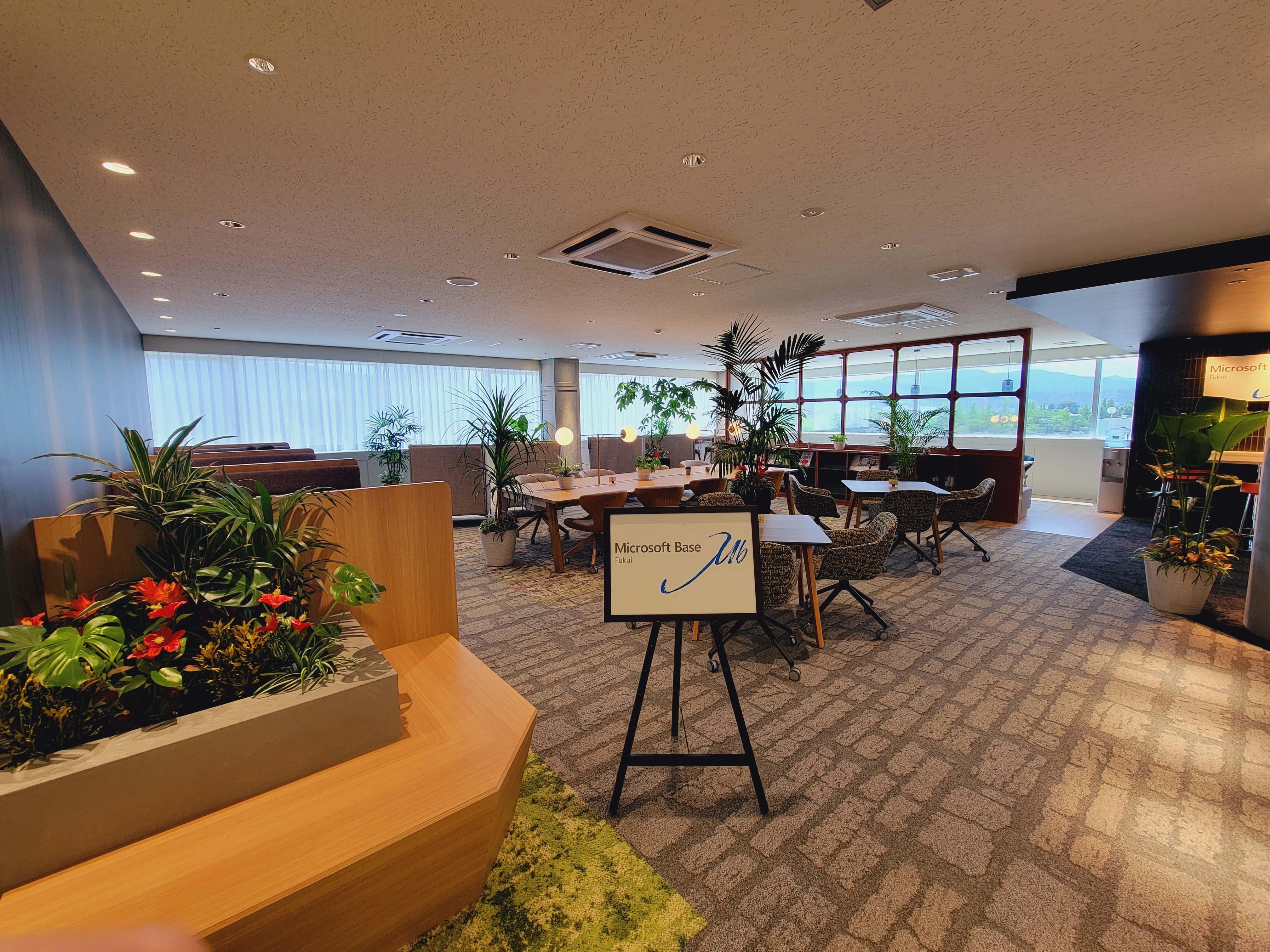 植物と多様な席が配置された広々としたラウンジ。立て看板に「Microsoft Base」と表示 Fukui。