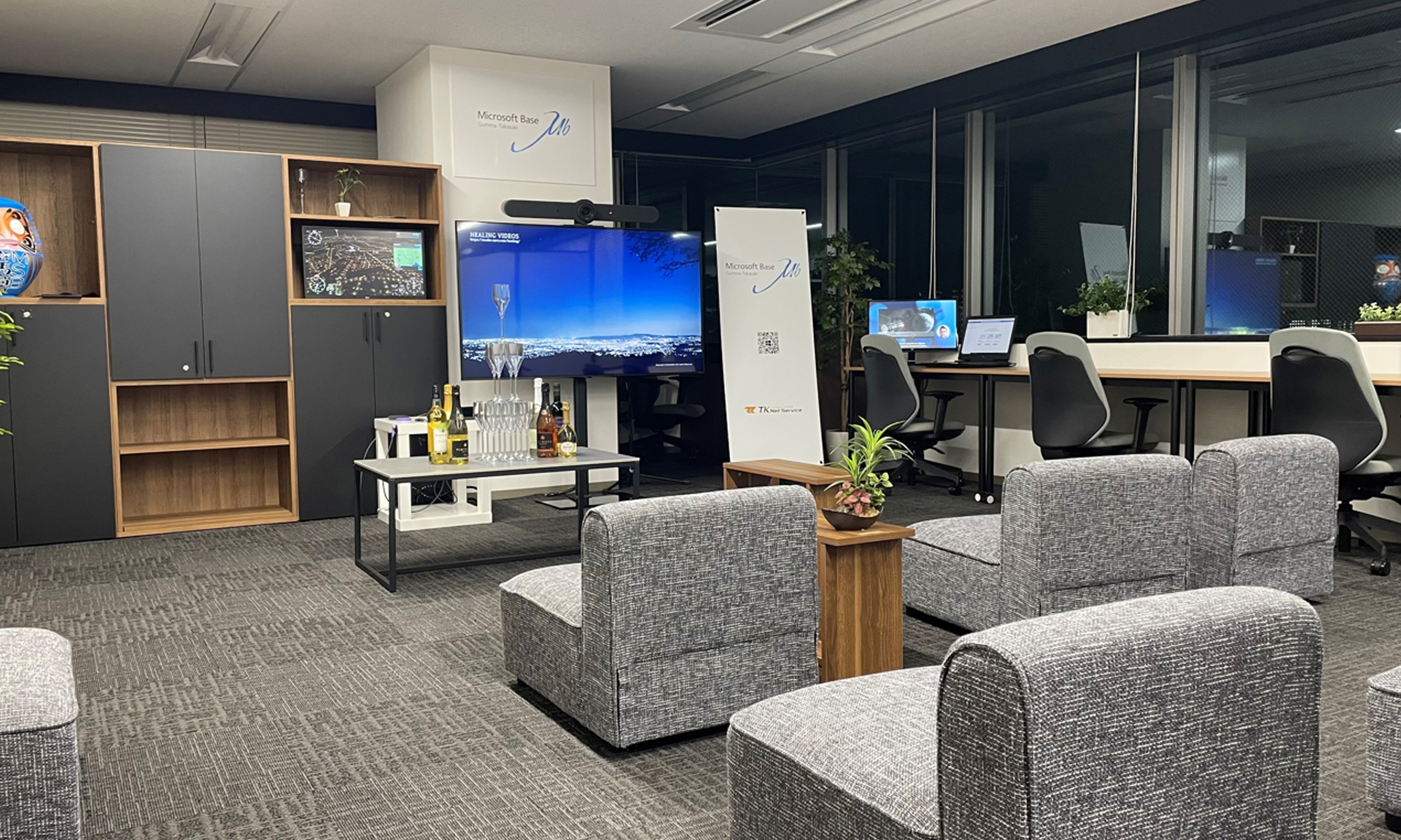 グレーのアームチェア、大型テレビ、奥にデスクワークスペースがあるモダンなラウンジエリア。