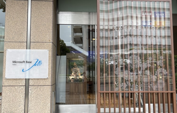縦格子の木製パネルがあるガラスの入口と、外壁の柱に「Microsoft Base Naha」と表示されたパネル。