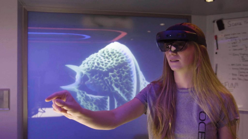 ラボ環境でHoloLensヘッドセットを装着し、3D海洋生物の投影を操作する女性。