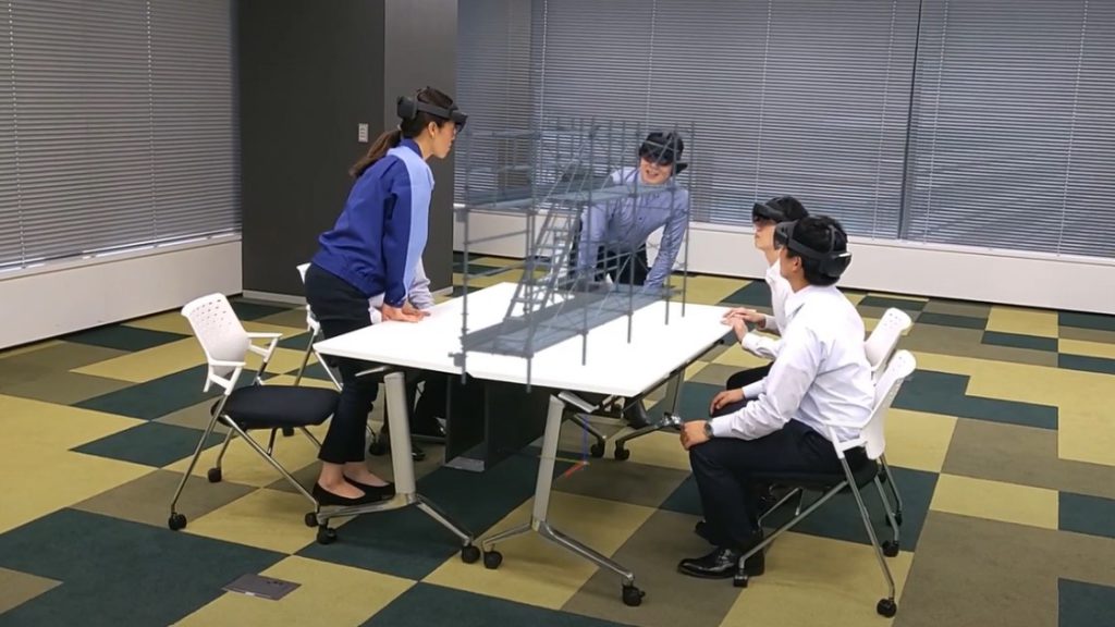 1 人の女性と 3 人の男性が、仮想マシンを装着したデジタル モデルについて話し合っています。