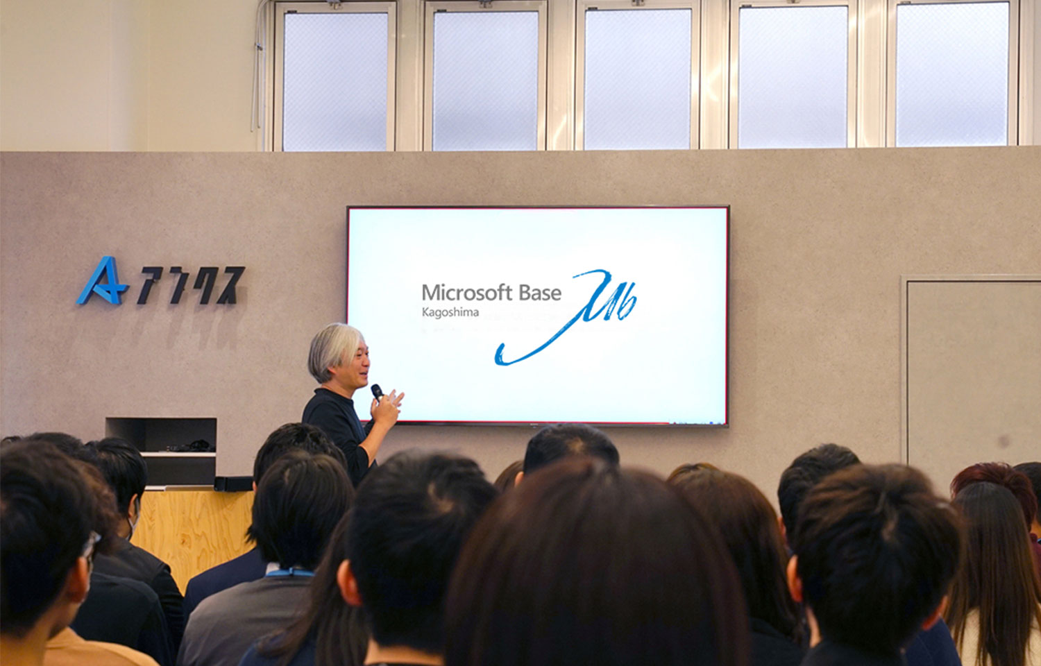 講師が聴衆に向けて話すセミナー空間、前方の大型スクリーンに「Microsoft Base Kagoshima」と表示。