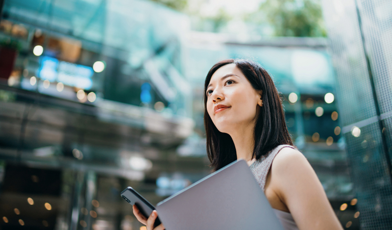 uma mulher segurando um notebook e um celular andando em um shopping