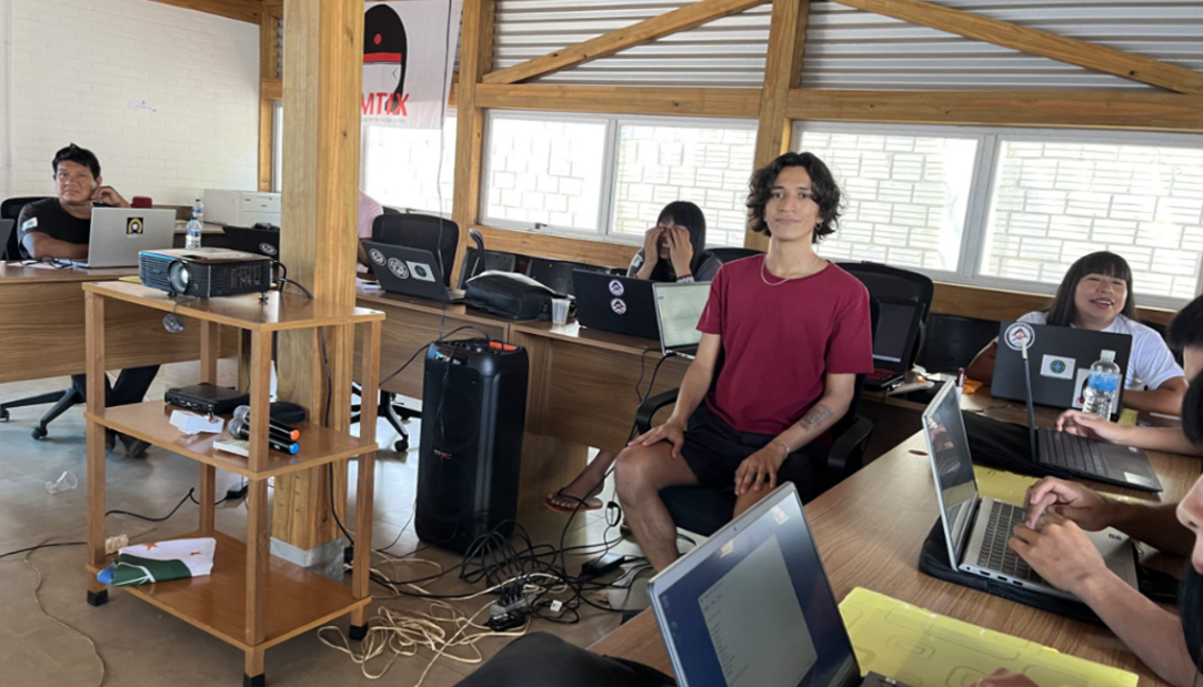 uma sala de aula com alunos utilizando notebooks e olhando para um projetor