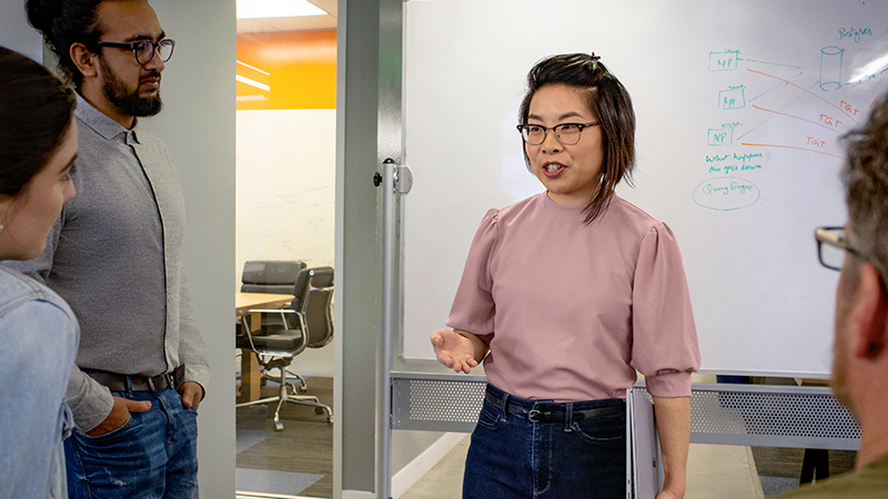 Desenvolvedora falando em frente a um quadro branco durante uma reunião em pé da equipe.