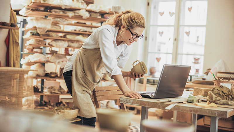 Uma ceramista usa um laptop em sua oficina.