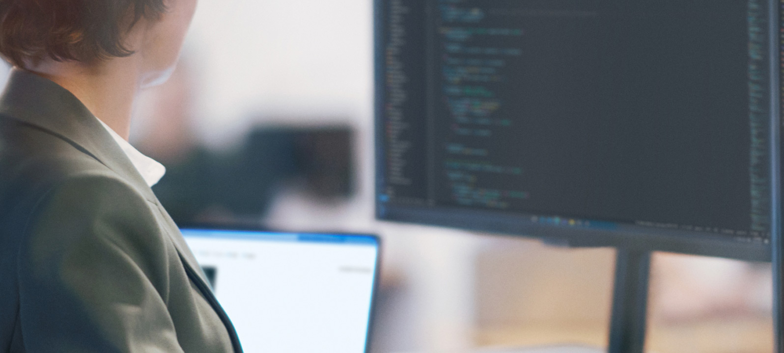 Um homem e uma mulher sentados olhando para um monitor onde uma mulher faz uma apresentação