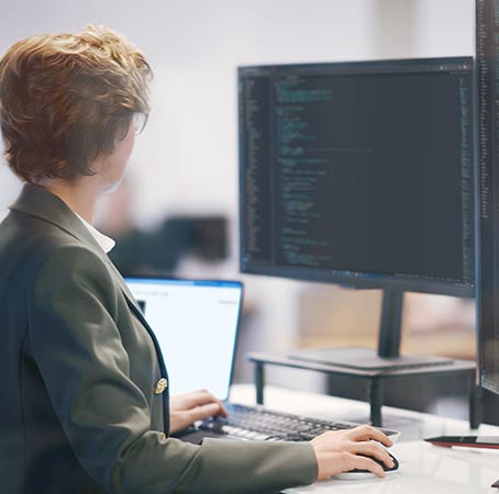 Um homem e uma mulher sentados olhando para um monitor onde uma mulher faz uma apresentação