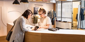 Duas mulheres em uma loja de roupas, enquanto uma delas usa um tablet