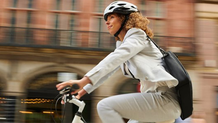 Woman on a bicycle with a helmet wearing full white with a black bag