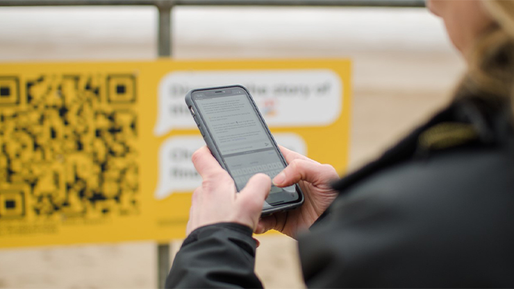 Person on their phone with a yellow sign with a QR code