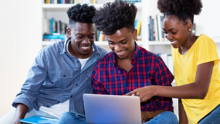 Three people looking and pointing at the laptop while smiling 